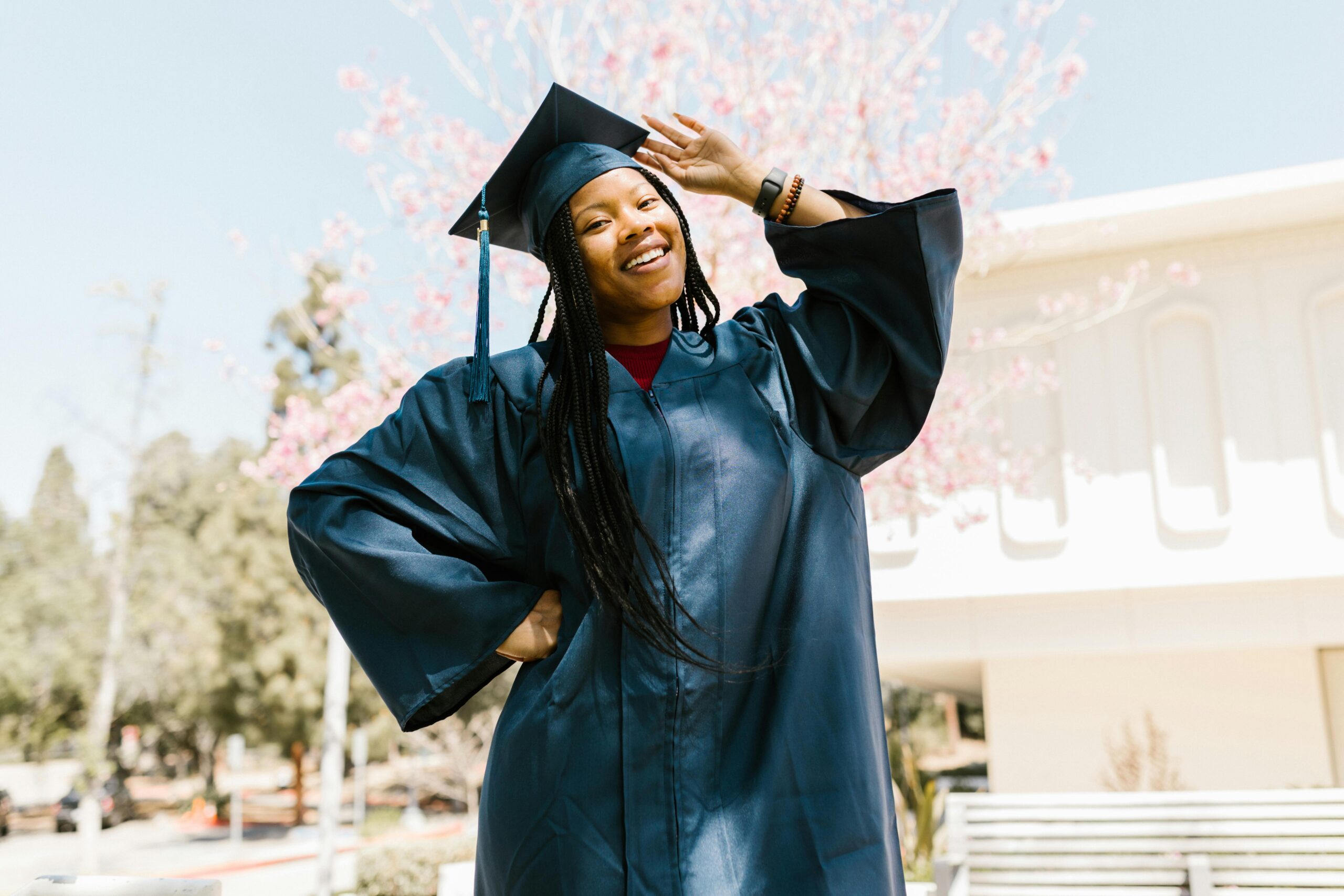 A joyful graduate poses outdoors in a blue cap and gown, celebrating success.